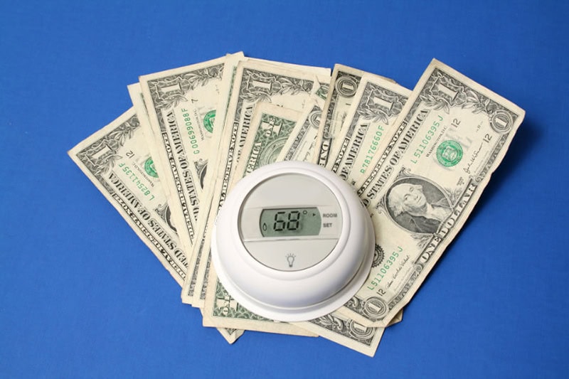 Spring Money-Saving Tips. A thermostat on a pile of money.