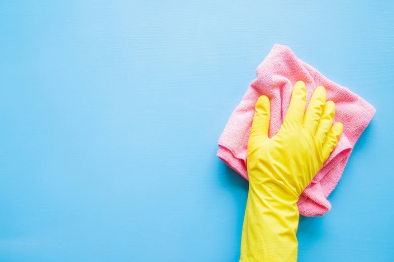 Does an AC Kill Mold? Photo of a hand in a yellow glove wiping a blue wall or table with a pink cloth.