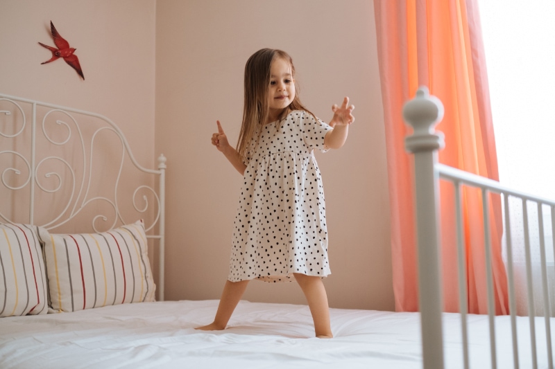Happy toddler girl in motion jumping on bed alone flying in air feeling joy.